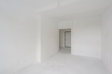 empty, all-white room with a doorway leading to another space. The walls are plain, and the floor is bare. Minimalist and clean aesthetic