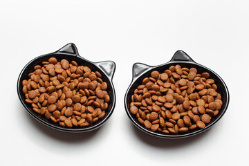Dry food in black ceramic bowl in shape of cat with ears, isolated on white background.
