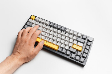 Top view of male hand typing on keyboard with grey and yellow key cap.