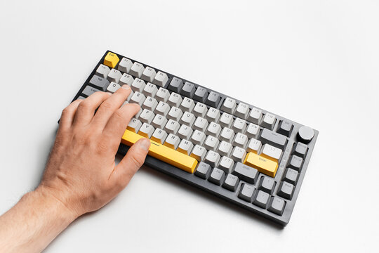 Top view of male hand typing on keyboard with grey and yellow key cap. - Powered by Adobe