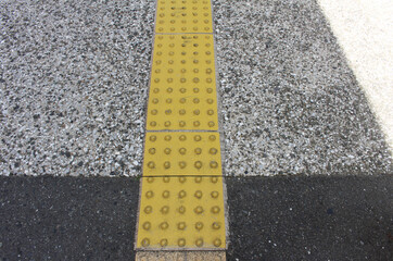 Yellow blocks of tactile paving for blind handicap. Tactile pavement for the visually impaired close up background. Texture of asphalt road with Braille blocks and white line in the street.