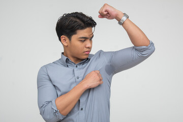 Southeast Asian man raising arm and inspecting visible armpit sweat stain, appearing embarrassed...