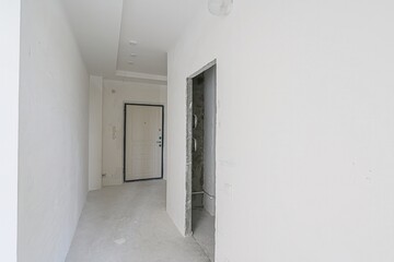 empty, all-white room with a doorway leading to another space. The walls are plain, and the floor is bare. Minimalist and clean aesthetic.