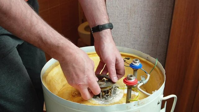 A worker holds a heating element of an electric boiler covered in rust and mineral deposits. Boiler maintenance and repair