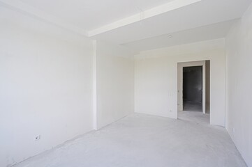 empty, all-white room with a doorway leading to another space. The walls are plain, and the floor...