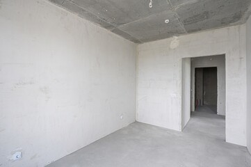 bright, empty room under construction. Concrete ceiling, plastered walls, and doorway opening to another unfinished space