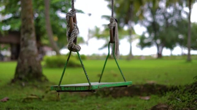 close up shot of an empty swing swinging by the wind blow under the tree with tight apperture