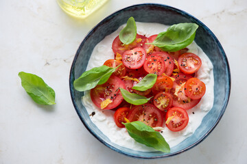 Blue bowl with stracciatella di bufala, cherry tomatoes and green basil on a light-beige marble background, horizontal shot, high angle view