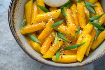 Bowl with korean traditional tteokbokki or rice cakes served in curry sauce, closeup, horizontal shot