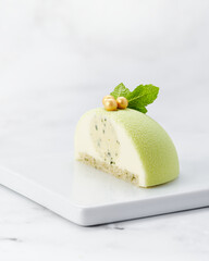 Elegant green velvet mousse cake cut in half, showing creamy filling with visible herbs. Served on white plate with marble background and copy space.