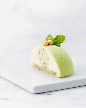 Elegant green velvet mousse cake cut in half, showing creamy filling with visible herbs. Served on white plate with marble background and copy space.
