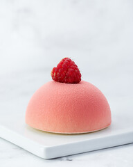 Elegant individual raspberry and white chocolate mousse cake with velvet texture and fresh raspberry on top. Served on white ceramic plate over marble background with copy space.