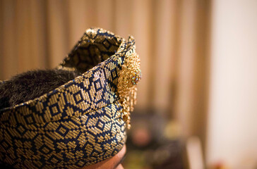 Obraz premium A portrait of the groom's accessories in an elegant Malay traditional attire in a Malay songket motif. Complete with Tanjak or head covering with sparkling gold accessories. Riau, Indonesia.