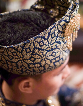A portrait of the groom's accessories in an elegant Malay traditional attire in a Malay songket motif. Complete with Tanjak or head covering with sparkling gold accessories. Riau, Indonesia.