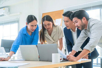 Group of business people reviewing financial charts and laptop insights while standing in office...