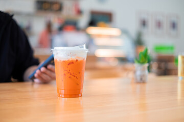 Ice Thai tea in clear plastic cup famous beverage drink traditional on wooden table in nature cafe, copy space