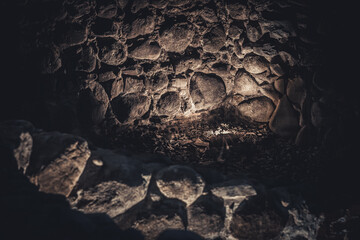 A moody, dimly lit stone wall surrounds a small niche with delicate white flowers, evoking a...