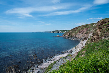 Fototapeta premium A scenic view of the coastline, showcasing the rugged cliffs meeting the tranquil blue sea under a bright, partly cloudy sky. 