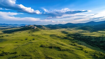 Fototapeta premium Serene aerial view of a vast, rolling green meadow landscape under a vibrant blue sky dotted with fluffy white clouds, showcasing distant mountains and a tranquil path. : Generative AI