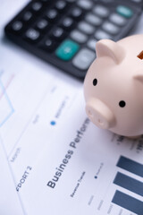 A piggy bank, calculator, and business performance report symbolize finance, savings, and financial analysis.