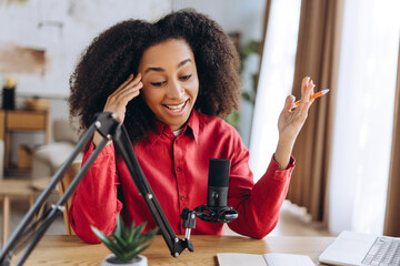 Young Latin woman recording podcast from home using microphone and laptop