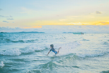 Joyful Ocean Plunge: A young child splashes and plays joyfully in the ocean waves at sunset, embracing the vibrant hues of the sky and the refreshing spray of the water.