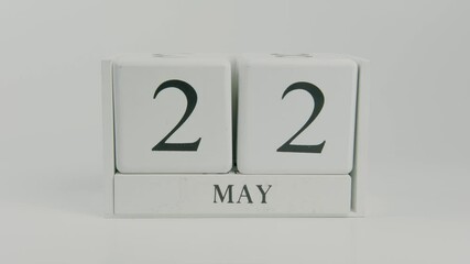 A hand flips a wooden calendar from May 22nd to May 23rd on a white background, symbolizing the passage of time and daily transitions