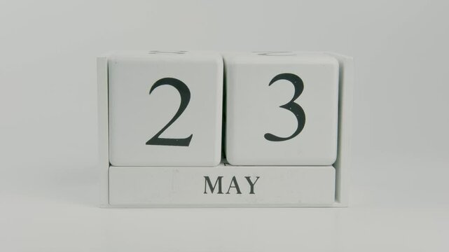 A hand flips a wooden calendar from May 23rd to May 24th on a white background, illustrating the transition between days and the ongoing flow of time