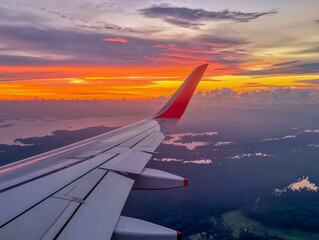Obraz premium As the sun begins to set, warm hues envelop the sky, casting a tranquil glow over the soft clouds below. This stunning view from an airplane wing inspires wanderlust and serenity