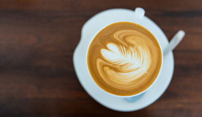A steaming cup of latte with latte art on a wooden table in a cozy cafe setting.