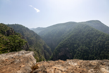 Green mountain valley with a rocky overlook under a bright sky. Scenic natural view.