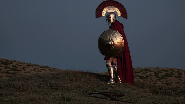 Muscular Spartan warrior standing heroically on rocky hill, wearing traditional bronze armor and holding spear against dramatic dusky evening sky, embodying ancient Greek military strength