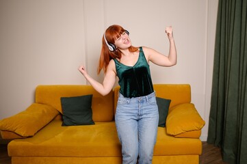 Woman relaxing at home after hard working week, listening to music on headphones. Cheerful girl...