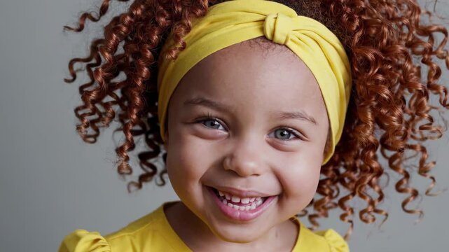 Joyful curly-haired girl in yellow outfit holding spring flowers and smiling brightly

