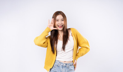Asian woman in yellow sweater pretends to listen to something interesting by raising one hand to...