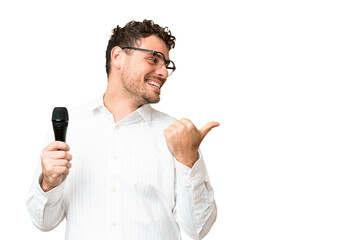 Brazilian man picking up a microphone over isolated chroma key background pointing to the side to...