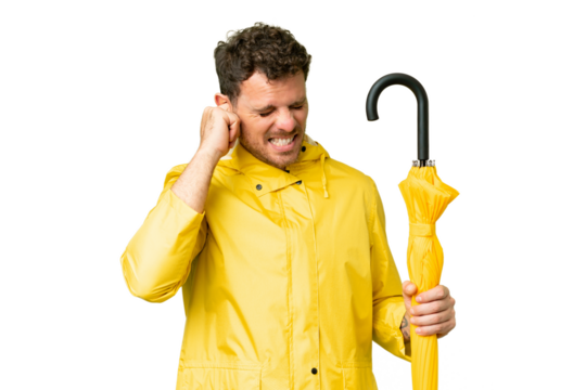 Brazilian man with rainproof coat and umbrella over isolated chroma key background frustrated and covering ears