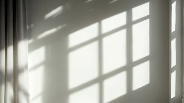 The light from the window shines on the white wall, as the curtain produces shadows, forming vague shapes and silhouettes.