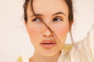 Close-up portrait of a young woman with natural makeup and freckles, looking away with hair gently...