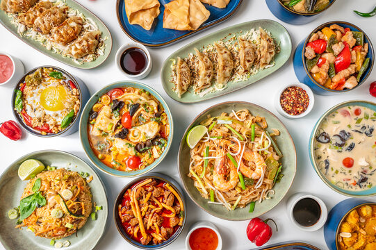 traditional Asian and Thai food with pad thai, dumplings, chicken soup and chicken krapao gai, served in ceramic bowls on a white background. Colorful and inviting top-down photo for culinary themes. 