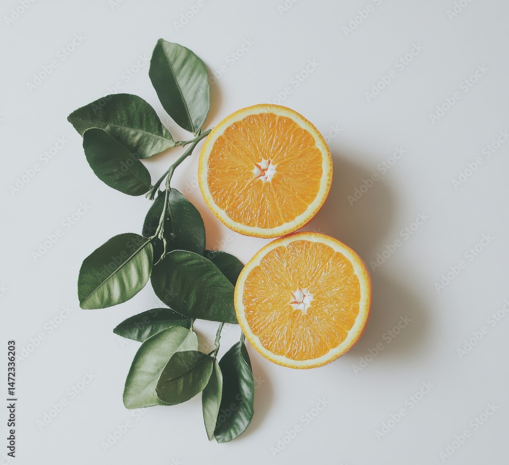 Poster two juicy orange halves, segmented and vibrant, rest beside a lush sprig of green citrus leaves on a
