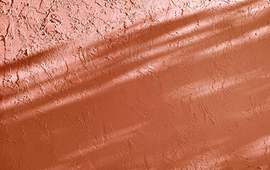 a textured brown wall is partially illuminated by diagonal sunlight shadows, creating an abstract...