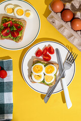Plate of toast with boiled eggs and avocado served on a plate on yellow background