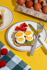 Plate of toast with boiled eggs and avocado served on a plate on yellow background