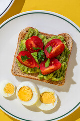Plate of toast with boiled eggs and avocado served on a plate on yellow background