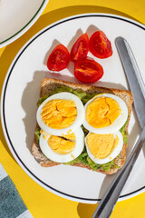 Plate of toast with boiled eggs and avocado served on a plate on yellow background
