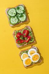 Delicious healthy bread toasts with fresh avocado, boiled eggs, cherry tomato and cucumber placed on bright yellow background
