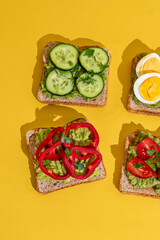 Delicious healthy bread toasts with fresh avocado, boiled eggs, cherry tomato and cucumber placed on bright yellow background