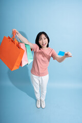 Young woman celebrating shopping success with colorful bags and credit card against a blue...