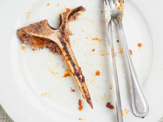 Finished high quality meal. Empty dirty plate with t bone, fork, knife. Fine dinner concept. Scraps...